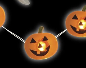 May include: A string of orange pumpkin-shaped lights against a black background. Each pumpkin features a carved jack-o'-lantern face with black triangular eyes, a triangular nose, and a wide, jagged mouth. The lights glow from within each pumpkin.