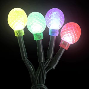 May include: A string of four multi-coloured LED lights. Each light is a different colour: yellow, green, purple, and red. The lights are round with a faceted design and sit atop black wires.