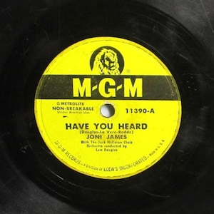 May include: A black vinyl phonograph record featuring a circular yellow center label with the MGM logo, a lion emblem, and the text Have You Heard by Joni James, with the Jack Halloran Choir and orchestra conducted by Lew Douglas, catalog 11390-A.