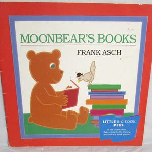 Pode incluir: Um livro infantil intitulado Moonbear's Books de Frank Asch com uma borda vermelha. A capa mostra um urso marrom lendo um livro vermelho, um pequeno pássaro com um chapéu preto e uma pilha de livros coloridos. Uma faixa azul na parte inferior diz Little Big Book Plus.