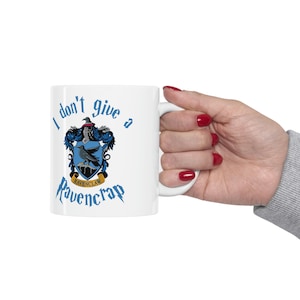 May include: White ceramic mug with a blue and gold Ravenclaw crest and the text "I don't give a Ravencrap".
