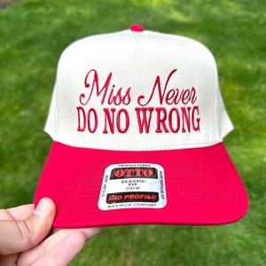 May include: A white and red baseball cap with the embroidered text "Miss Never Do No Wrong." The cap has a red brim and a white crown. The cap has a sticker that says "Classic Fit OSFM".