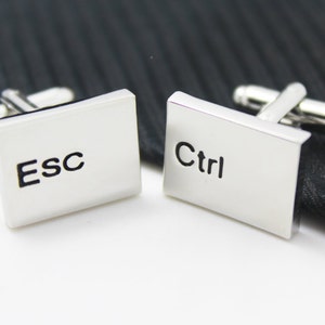 Può includere: Gemelli d'argento con facce rettangolari. Un gemello dice "ESC" e l'altro dice "Ctrl".
