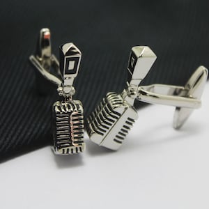 May include: A pair of silver cufflinks shaped like vintage microphones. The microphones have a silver finish and black details.