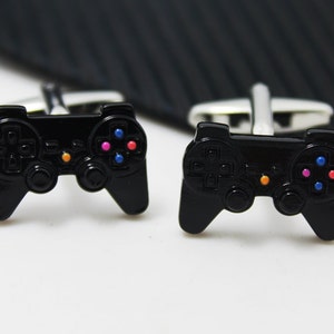 May include: A pair of black metal cufflinks shaped like a video game controller. The controller has colorful buttons.