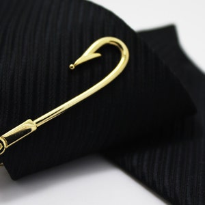 May include: A gold-coloured tie clip shaped like a fish hook. The clip is on a black tie.