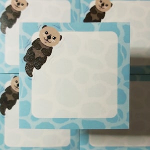 May include: A blue and white patterned note card with a cartoon sea otter illustration. The otter is brown and has a white belly. The card has a blank white space for writing.