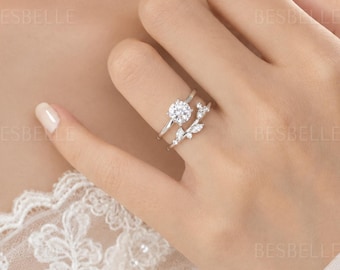 Op de afbeelding: Een zilverkleurige ringenset bestaande uit een solitaire ring met een rond geslepen middensteen en een bijpassende ring met een bladvormig ontwerp en kleine accentstenen. Het sieraad wordt om de vinger gedragen en toont het fijne metaalwerk.
