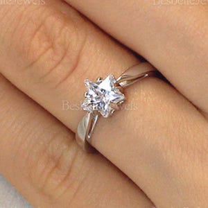 May include: A silver ring featuring a star-shaped, clear gemstone. The ring is set on a slender band and is shown on a person's finger. The brand name "Besbelle Jewels" is visible in the background.