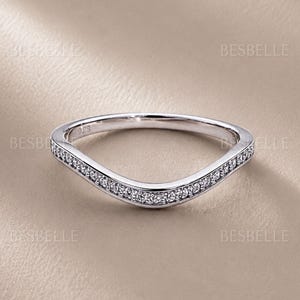 May include: A silver-toned curved ring featuring a row of small, clear pavé-set stones along the front band. The interior of the band is clearly stamped with the text 925, indicating sterling silver composition. The brand name BESBELLE is visible.