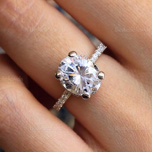 May include: A silver engagement ring with a large oval-shaped diamond. The diamond is set in a prong setting and has a halo of smaller diamonds. The band is also set with smaller diamonds.