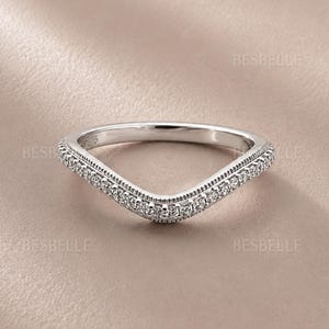 May include: A silver-toned chevron-shaped ring featuring a row of small, clear, round-cut stones set along the outer edge. The band has a milgrain texture detail bordering the stones. The text BESBELLE is visible multiple times in the image.