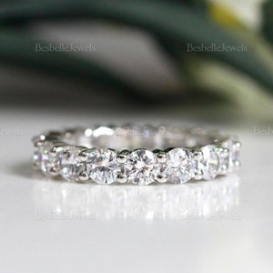 May include: A close-up of a silver eternity ring with multiple round-cut, clear gemstones. The ring is set on a white surface. The brand name "BesbelleJewels" is visible in the background.