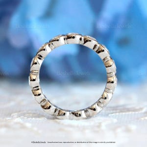May include: A silver ring with a continuous row of small, clear gemstones. The ring has a textured, scalloped design along the band. The words "Besbelle Jewels" are visible in the image.
