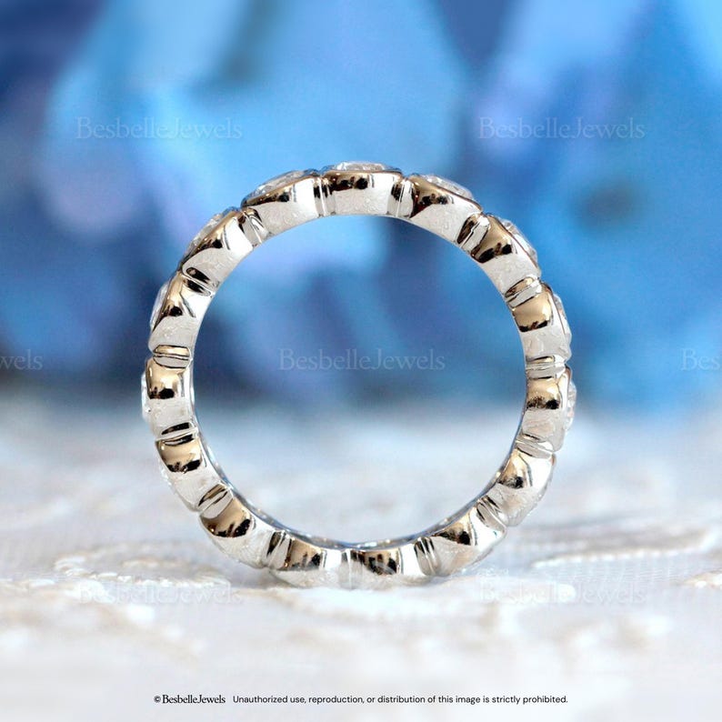 May include: A silver ring with a continuous row of small, clear gemstones. The ring has a textured, scalloped design along the band. The words "Besbelle Jewels" are visible in the image.