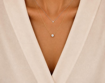 Può includere: Un set di collane a strati composto da due catenine delicate. La catenina più corta è color argento con una piccola pietra rotonda, mentre la catenina più lunga è color oro con un ciondolo centrale a forma di pietra rotonda sfaccettata.