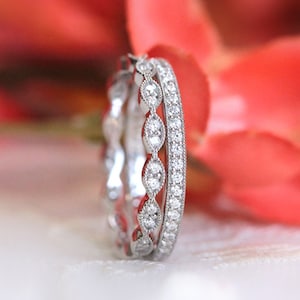 Op de afbeelding: Twee zilveren trouwringen met een rij kleine diamanten. De ring aan de linkerkant heeft een meer bewerkt ontwerp met grotere diamanten.