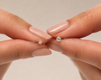 Puede incluir: Dos pendientes de botón con piedra redonda de talla brillante en metal plateado. Un pendiente está etiquetado como 2,0 mm y el otro como 3,0 mm, indicando sus diámetros. Cada pendiente presenta una piedra clara sujeta por tres garras.