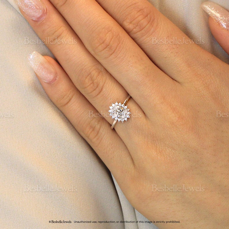 May include: A silver ring with a large oval-cut center stone surrounded by smaller, round accent stones. The ring is set on a slender band and is displayed on a hand.