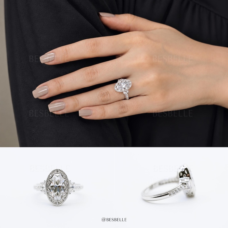 May include: A silver-toned ring featuring a central marquise-cut stone surrounded by a halo of smaller round stones. The band includes intricate milgrain detailing along the edges and additional small stones set along the shank of the ring.