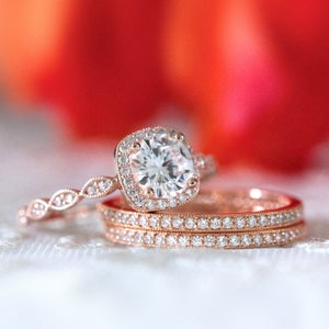 May include: A rose gold engagement ring set with a large, square-cut diamond surrounded by smaller diamonds. The ring is paired with two delicate rose gold bands.