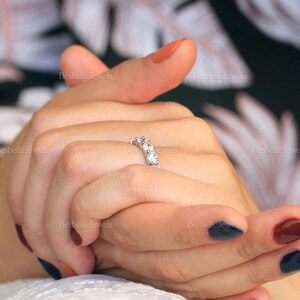 May include: A silver ring with five clear gemstones. The ring is set on a woman's hand with painted nails. The background is a floral pattern. The text "BesbelleJewels" is visible in the background.