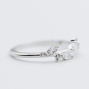 May include: A silver ring with a leaf-inspired design, set with clear gemstones. The ring features marquise and round cut stones, creating a delicate and elegant look. The ring is displayed on a white background, showcasing its intricate details.