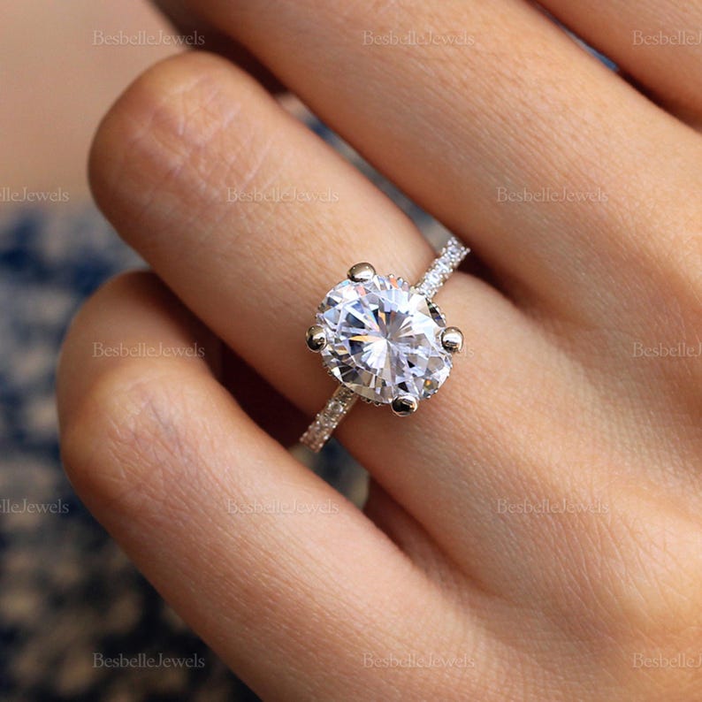May include: A silver engagement ring with a large oval-shaped diamond. The diamond is set in a prong setting and has a halo of smaller diamonds. The band is also set with smaller diamonds.