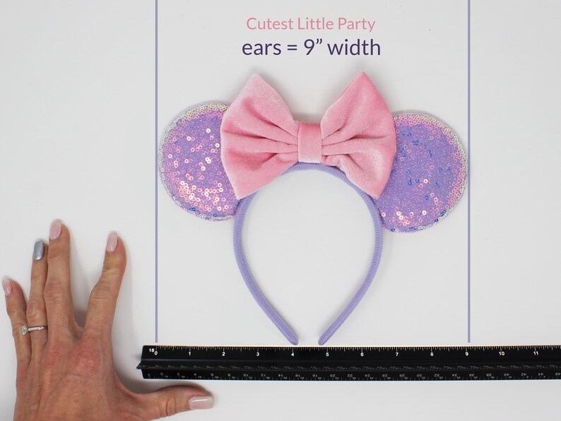 May include: A headband featuring two circular ears covered in iridescent purple sequins and a large, central pink velvet bow. The text Cutest Little Party ears = 9" width is visible above the headband, which is positioned next to a black ruler.