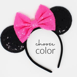May include: A black headband featuring two circular ears covered in black sequins and a large, bright pink bow with subtle sequin accents. The text "choose color" is printed in black in the center of the headband between the ears.