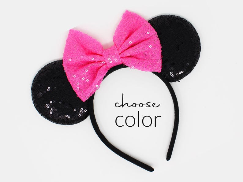 May include: A black headband featuring two circular ears covered in black sequins and a large, bright pink bow with subtle sequin accents. The text "choose color" is printed in black in the center of the headband between the ears.