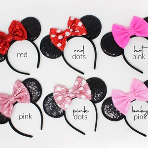 May include: Six headbands with black sequined ears and fabric bows in various colors and patterns. The bows are labeled red, red dots, hot pink, pink, pink dots, and baby pink. Each headband features a thin black band and round ears.