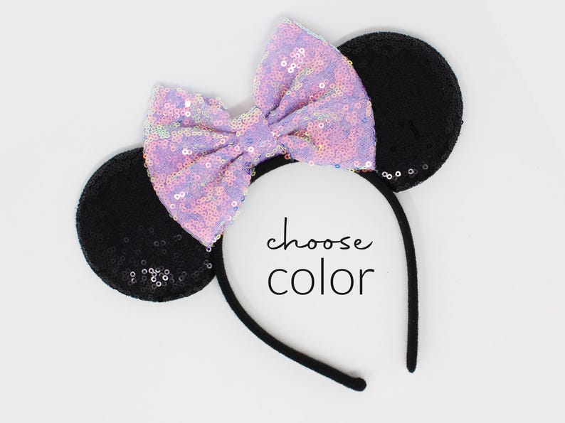 May include: A headband featuring two round black sequined ears and a large, central lavender sequined bow. The text "choose color" is printed in black in the center of the headband. The headband frame is thin and black.