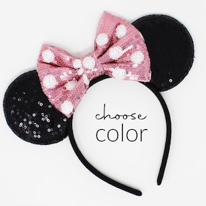 May include: A headband featuring two round black sequined ears and a large pink sequined bow with white polka dots. The center of the headband displays the text choose color in a black script and sans-serif font combination.
