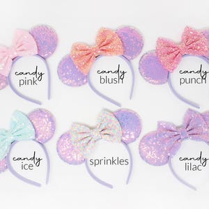 May include: Six headbands with round ears covered in iridescent purple sequins and fabric bows. The bows are labeled candy pink, candy blush, candy punch, candy ice, sprinkles, and candy lilac. Each headband features a thin, light purple band.