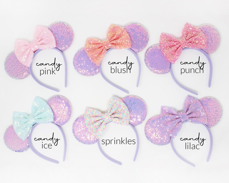 May include: Six headbands with round ears covered in iridescent purple sequins and fabric bows. The bows are labeled candy pink, candy blush, candy punch, candy ice, sprinkles, and candy lilac. Each headband features a thin, light purple band.