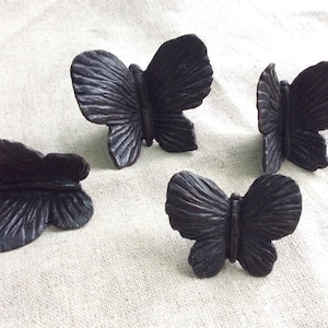 May include: Four black ceramic butterfly napkin rings. The rings are detailed with textured wings and a smooth body.