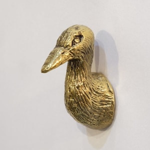May include: A gold-colored metal duck head door knocker with a textured surface.