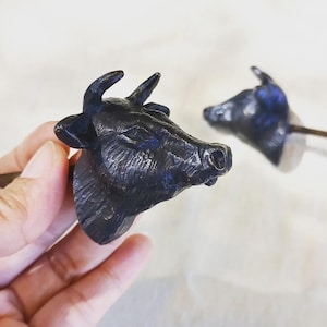 Peut inclure: Deux tirettes de tiroir en métal noir en forme de tête de vache. Les têtes de vache sont détaillées et réalistes.