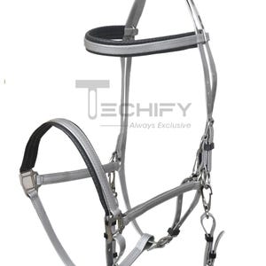 Puede incluir: Cabezada de caballo plateada y negra con testera y muserola acolchadas. La cabezada presenta herrajes metálicos y correas de cuero. El texto "TECHIFY Always Exclusive" es visible.