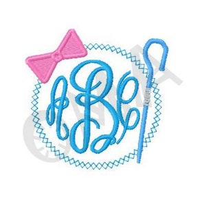 May include: A blue monogram with a pink bow and a blue shepherd's crook in a circle with a blue and white border.