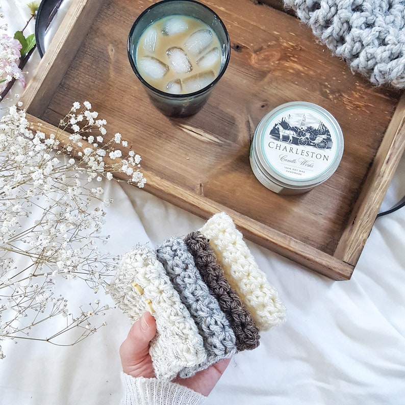 May include: A set of five crocheted dishcloths in various shades of brown, gray, and white. The dishcloths are stacked on top of each other and are being held by a hand. The dishcloths are on a white surface.