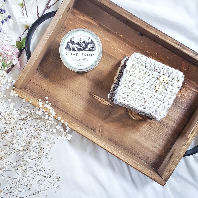 May include: A wooden tray with a crocheted square and a round tin with the text "Charleston Candle Works" on it.