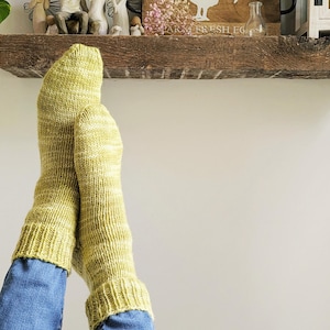Peut inclure: Paire de chaussettes tricotées à la main, vert clair et blanc moucheté. Les chaussettes sont tirées sur un jean bleu, avec des poignets côtelés aux chevilles. Les chaussettes semblent douces et chaudes.