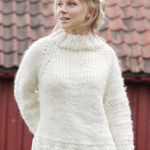 May include: A chunky knit sweater in an off-white color featuring a high mock neck collar, long sleeves with raglan seams, and a ribbed hem. The garment is crafted from a thick, textured yarn with a visible stitch pattern throughout the body.