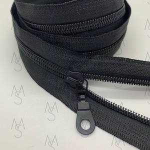 May include: Black zipper tape with a black zipper pull. The zipper tape is folded and stacked on a white surface.