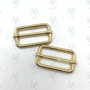 May include: Two gold-toned metal slider buckles. The buckles are rectangular with a smooth finish and two parallel bars.