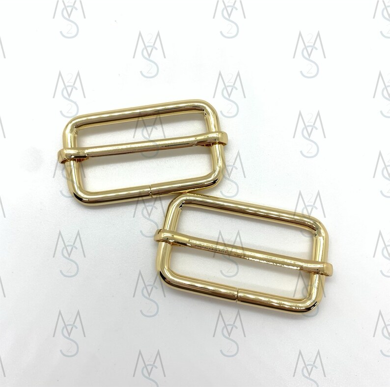 May include: Two gold-toned metal slider buckles. The buckles are rectangular with a smooth finish and two parallel bars.