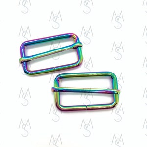 May include: Two iridescent rainbow-colored metal slider buckles. The buckles are rectangular with a rounded edge and have a smooth, shiny finish.