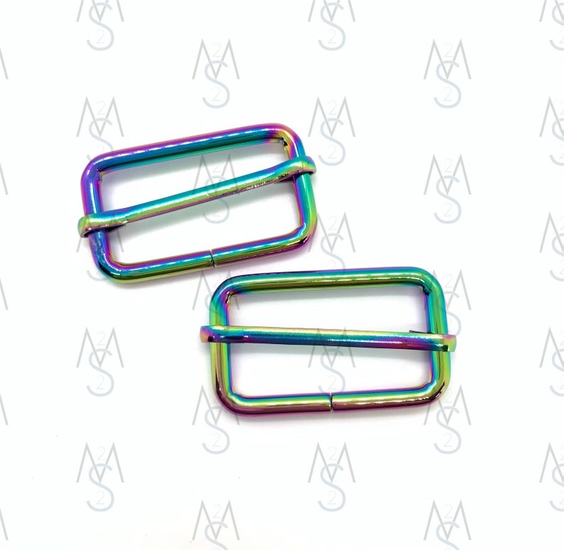 May include: Two iridescent rainbow-colored metal slider buckles. The buckles are rectangular with a rounded edge and have a smooth, shiny finish.